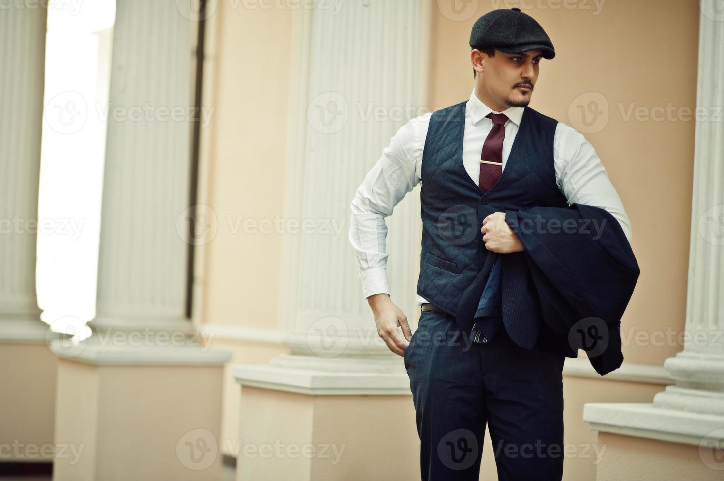 Portrait of retro 1920s english arabian business man wearing dark suit, tie and flat cap. photo
