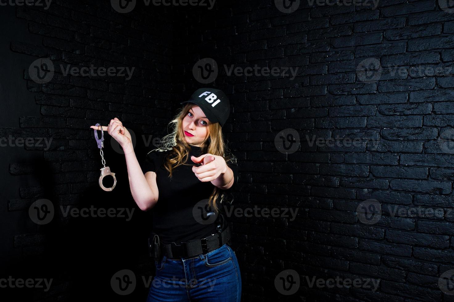 FBI female agent in cap and with gun at studio against dark brick wall. photo