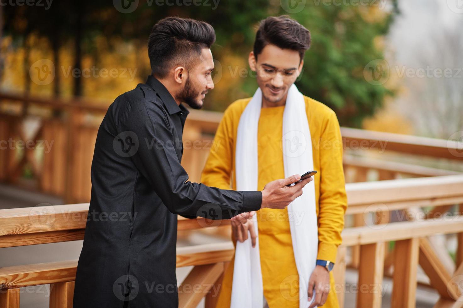 Two indian stylish mans friends in traditional clothes posed outdoor and looking on mobile phone. photo