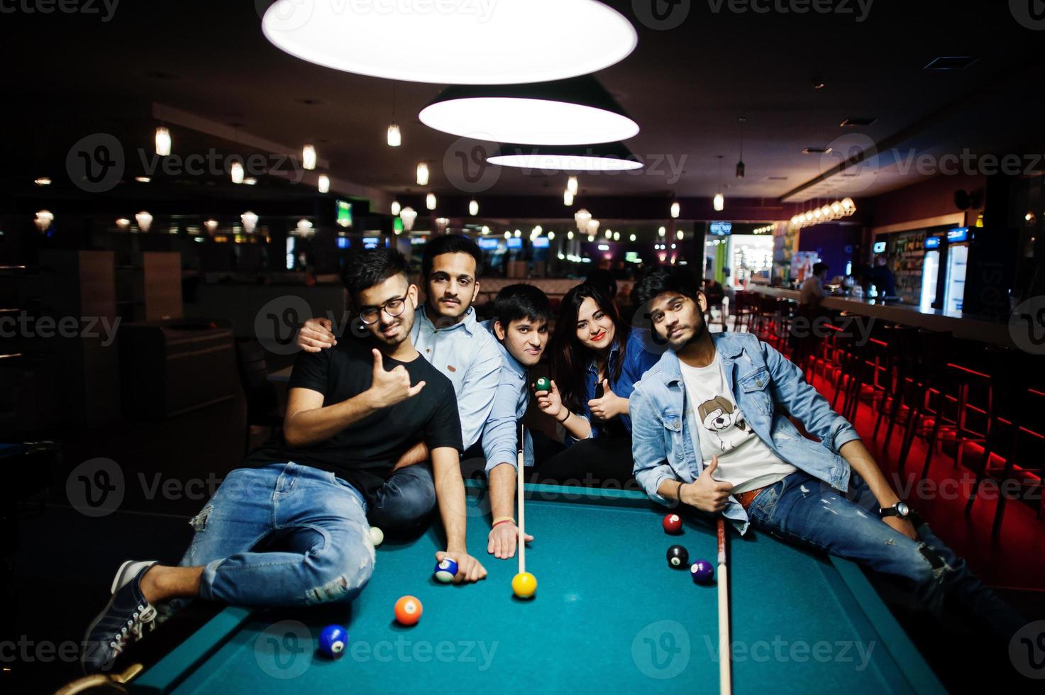 Group of stylish asian friends wear on jeans playing pool billiard on bar. photo