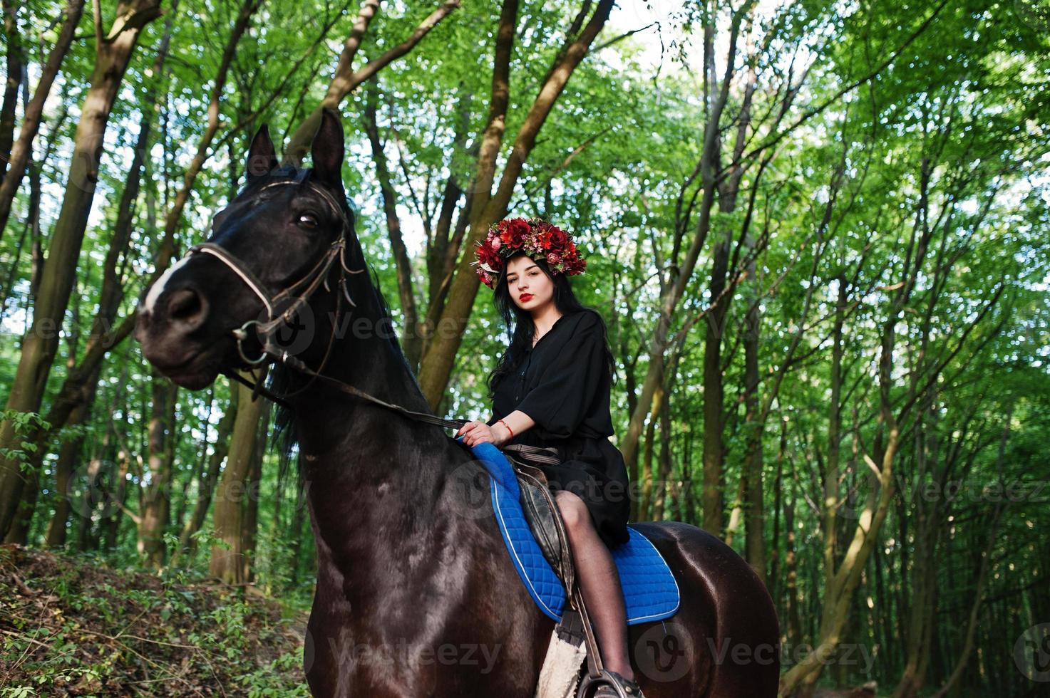 Mystical girl in wreath wear in black at horse in wood. photo