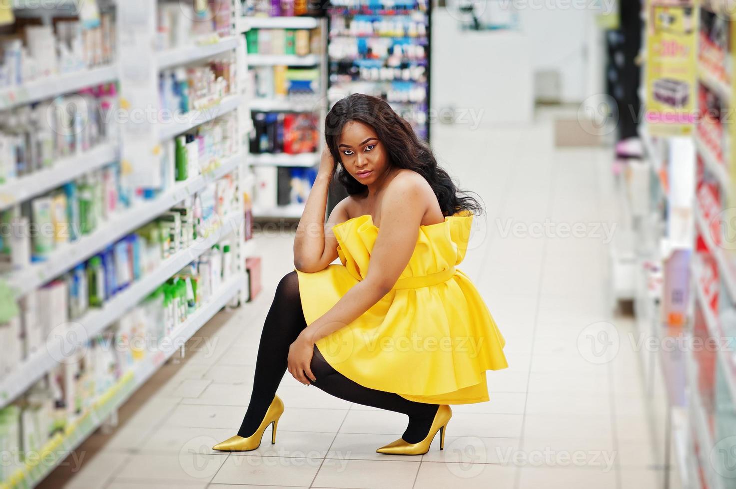 Elegante mujer afroamericana vestida de amarillo posada en una tienda de cosméticos, comprando accesorios de maquillaje en un salón de belleza. foto