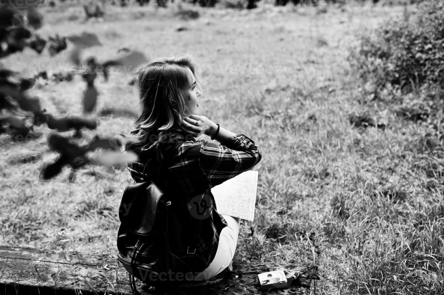 Portrait of a positive young gorgeous blonde sitting on the ground with a map in her hands in the forest. photo