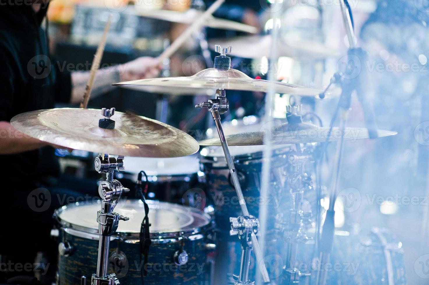 el baterista toca la batería en el escenario en una sala de conciertos detrás de una pared de vidrio. foto