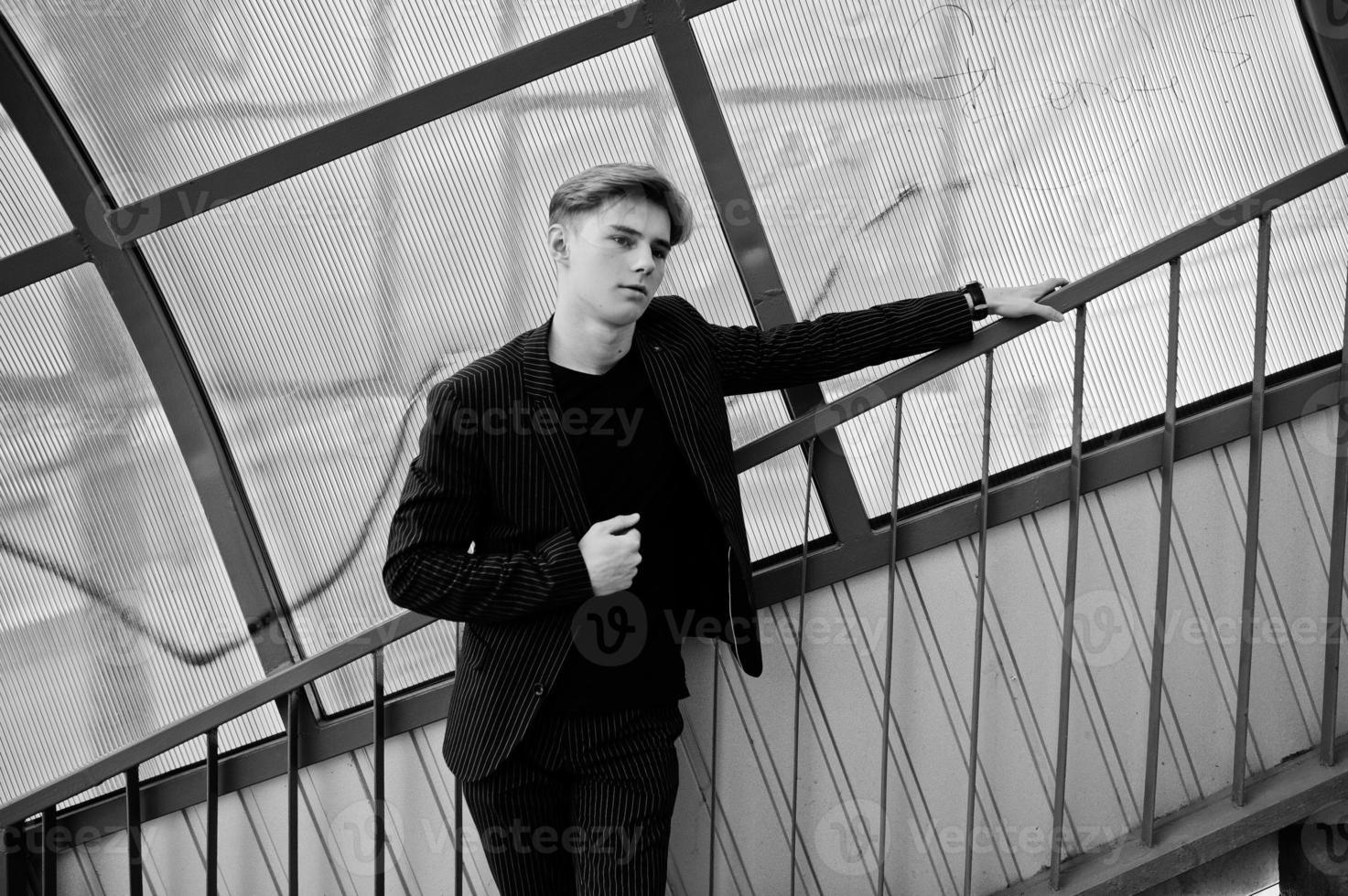 Young stylish macho boy in black jacket posed outdoor of street. Amazing model man at red stairs tonnel. photo