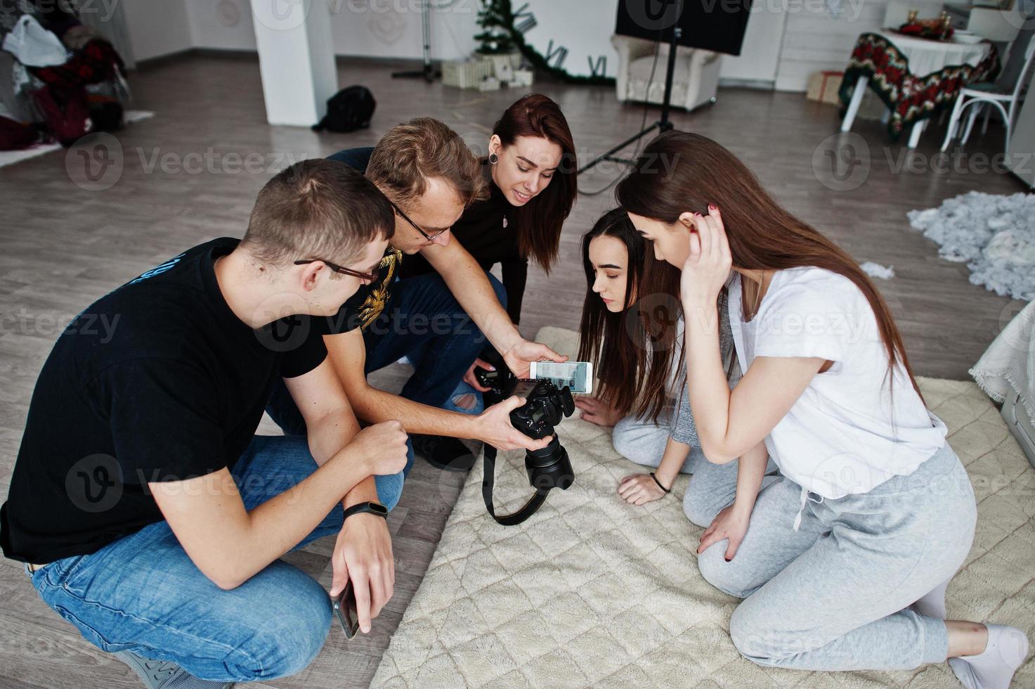 The team of photographers showing pictures on screen of camera for twins models girls on studio. Professional photographer on work. photo