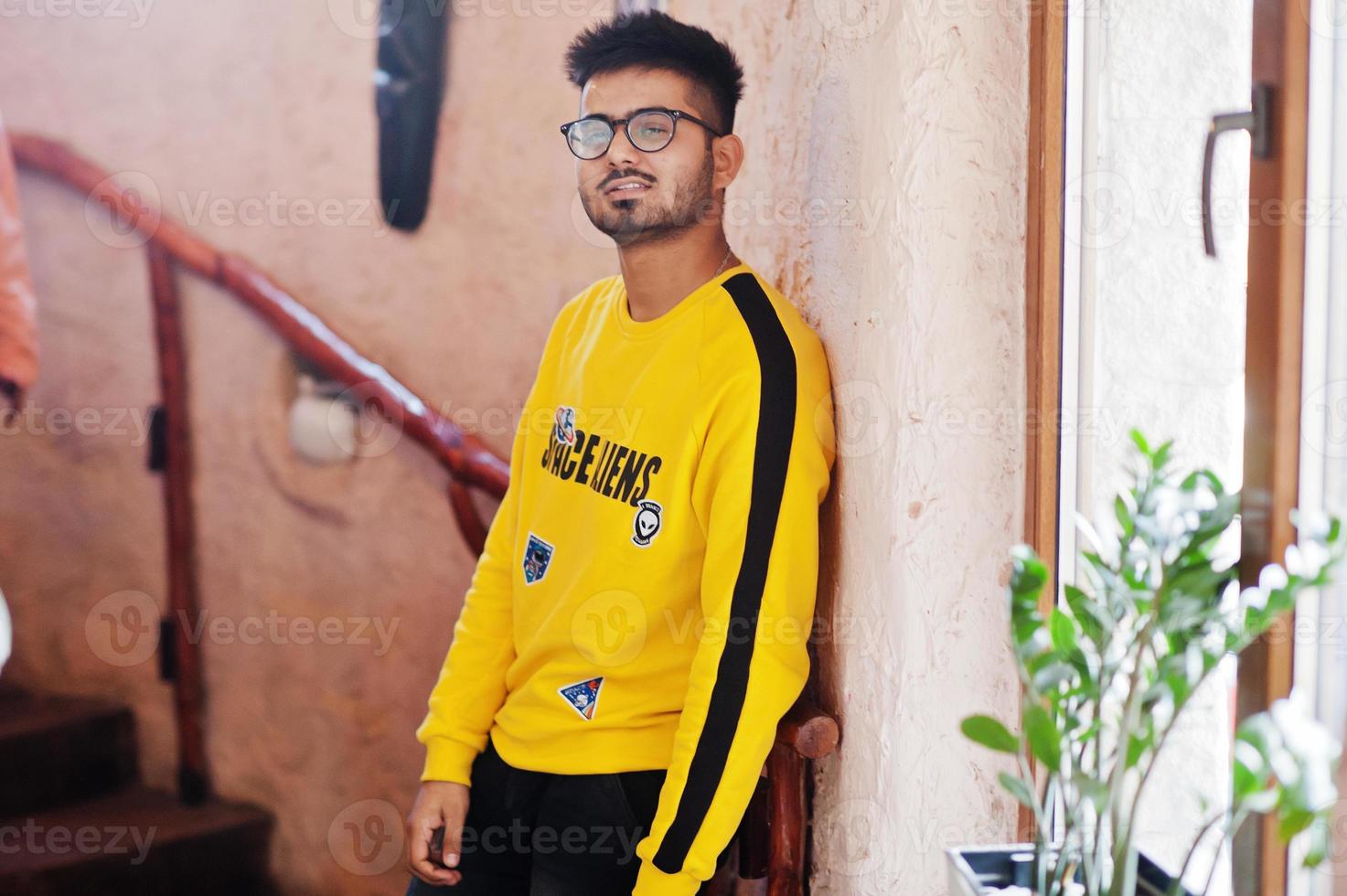 Asian man in eyewear and yellow sweatshirt posing indoor stairs of house against window. photo