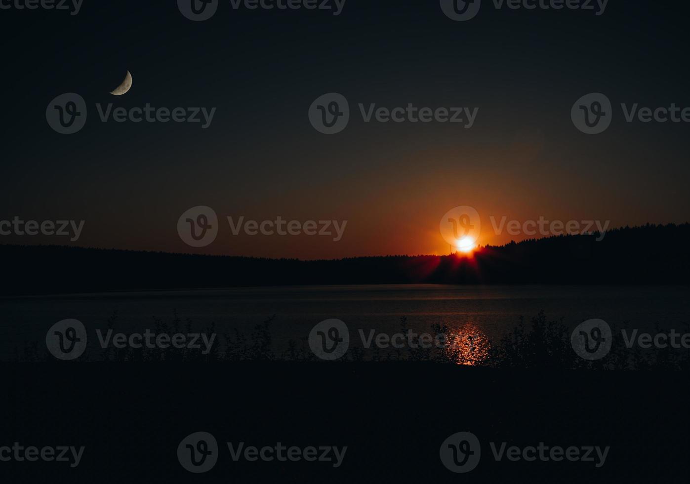 anochecer sobre un lago con luna y sol foto