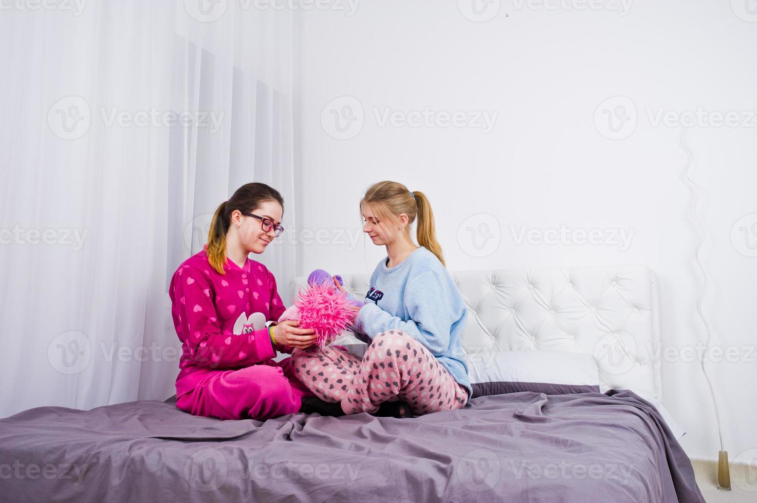 Two friends girls in pajamas having fun on bed at room. photo