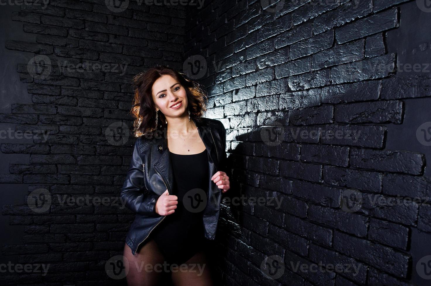retrato de estudio de chica morena sexy en chaqueta de cuero negro contra la pared de ladrillo. foto
