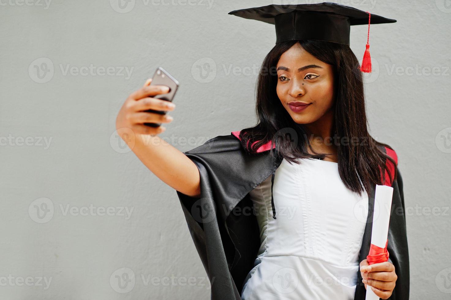 joven estudiante afroamericana con diploma y teléfono móvil posa al aire libre. foto