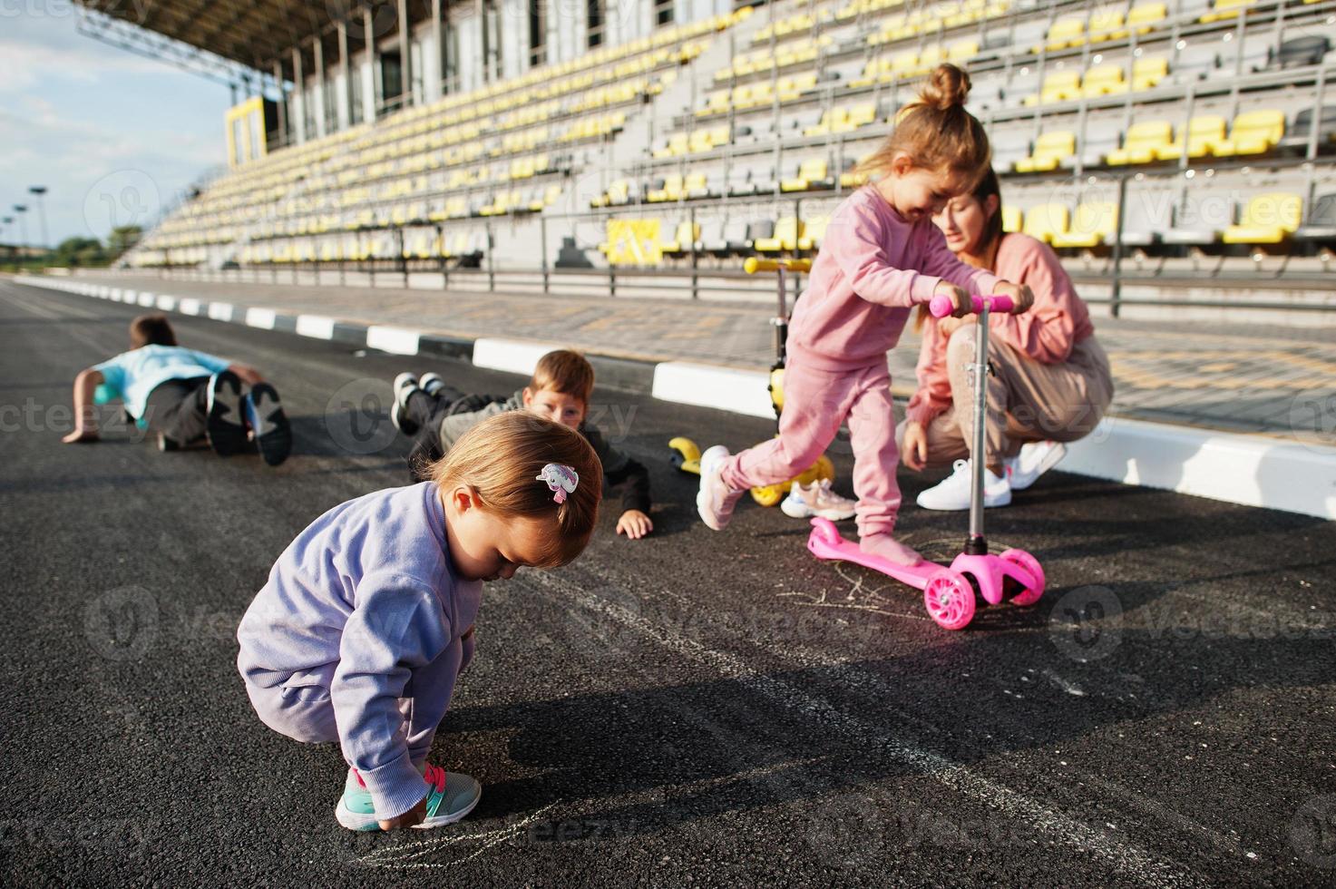 Young stylish mother with four kids outdoor. Sports family spend free time outdoors with scooters and skates. Painted with chalk on the asphalt. photo