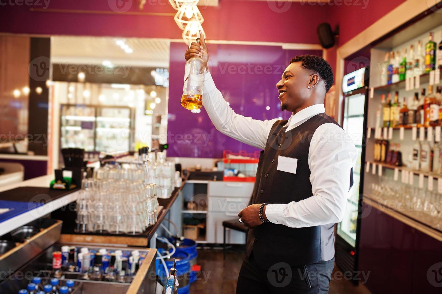 African american bartender at bar holding bootle. Alcoholic beverage preparation. photo