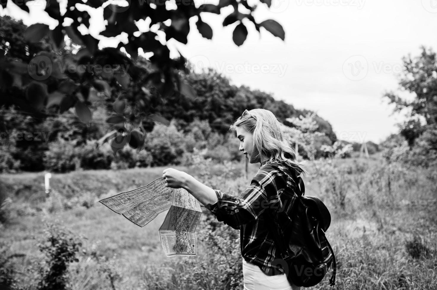 retrato de una hermosa chica rubia con camisa de tartán caminando con un mapa en el campo. foto