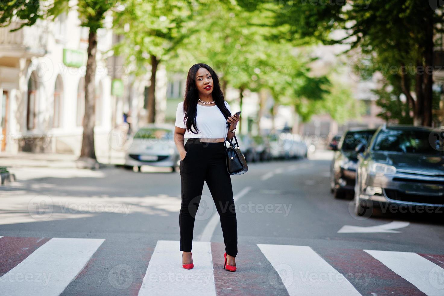 Stylish african american business woman on streets of city at pedestrian crossing. photo