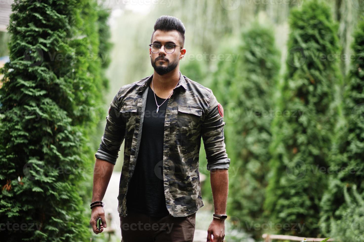 Awesome beautiful tall ararbian beard macho man in glasses and military jacket posed outdoor. photo