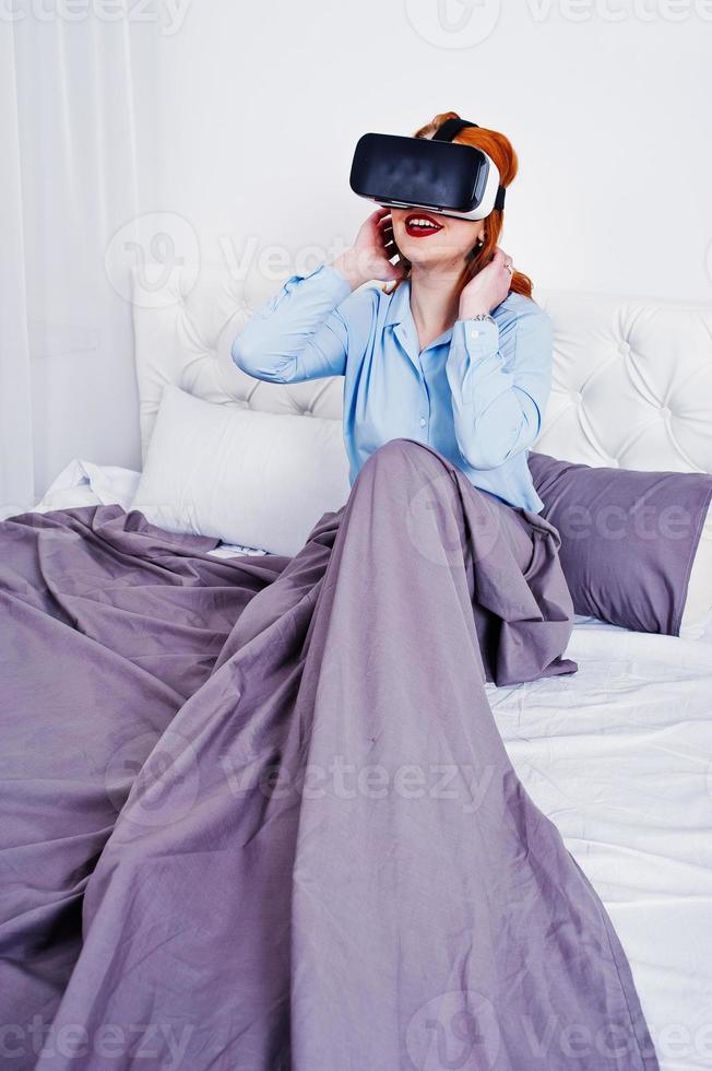 Red haired girl in bed with vr glasses at studio room. photo