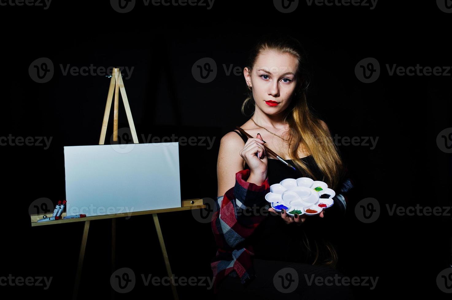 Beautiful woman artist painter with brushes and oil canvas posing in studio isolated on black. photo