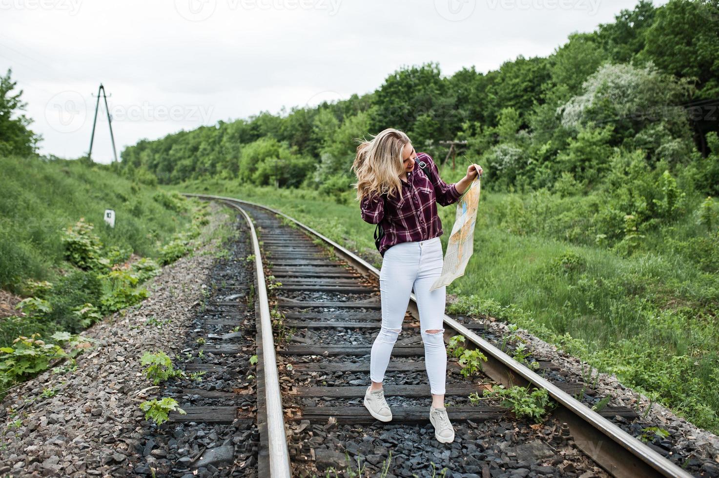 retrato de una linda chica rubia con camisa de tartán caminando por el ferrocarril con un mapa en las manos. foto