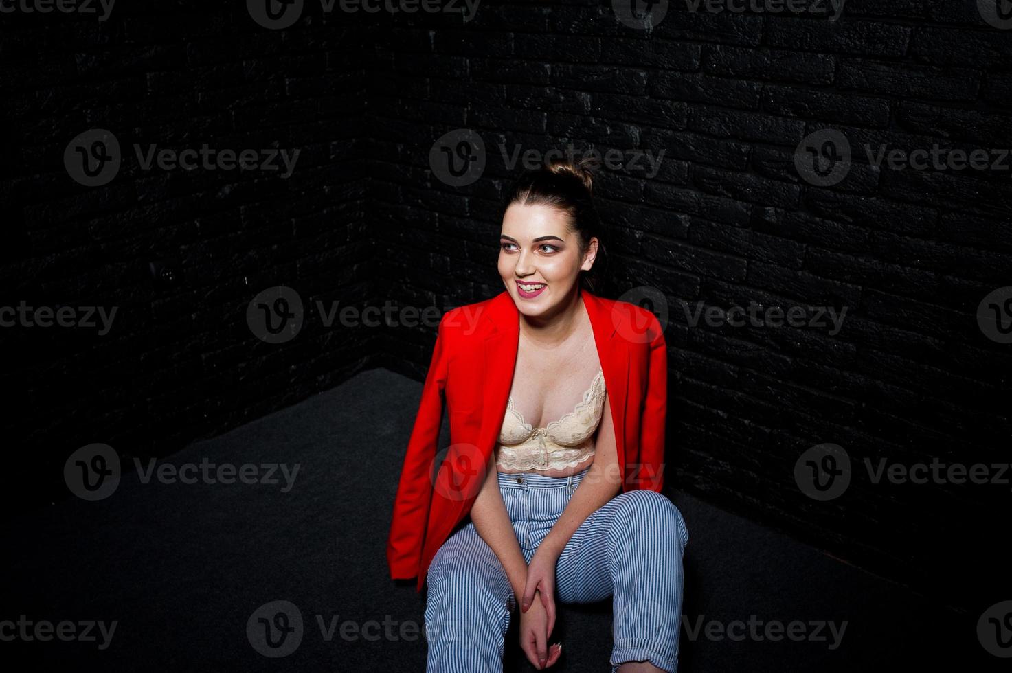 chica morena con estilo en chaqueta roja contra la pared de ladrillo negro de estudio. foto