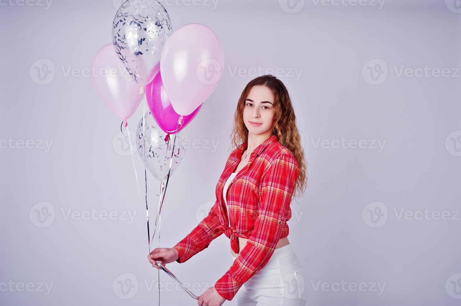 Young girl in red checked shirt and white pants with balloons against white background on studio. photo