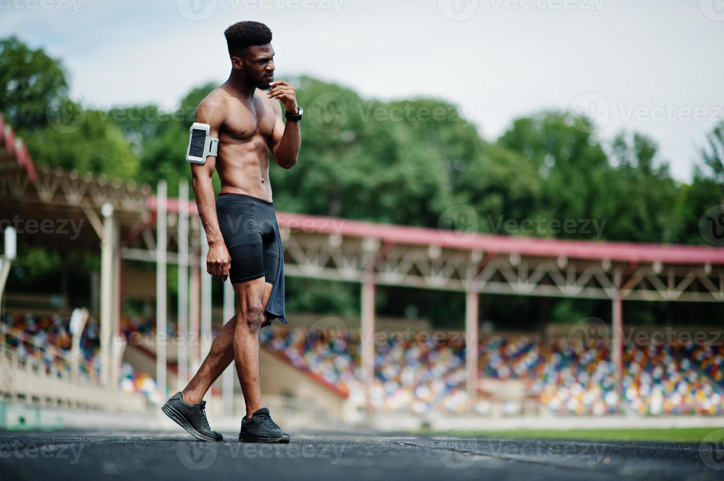 African american male athlete sexy sport bare torso man with running sports arm case for mobile phone, posed at stadium. photo