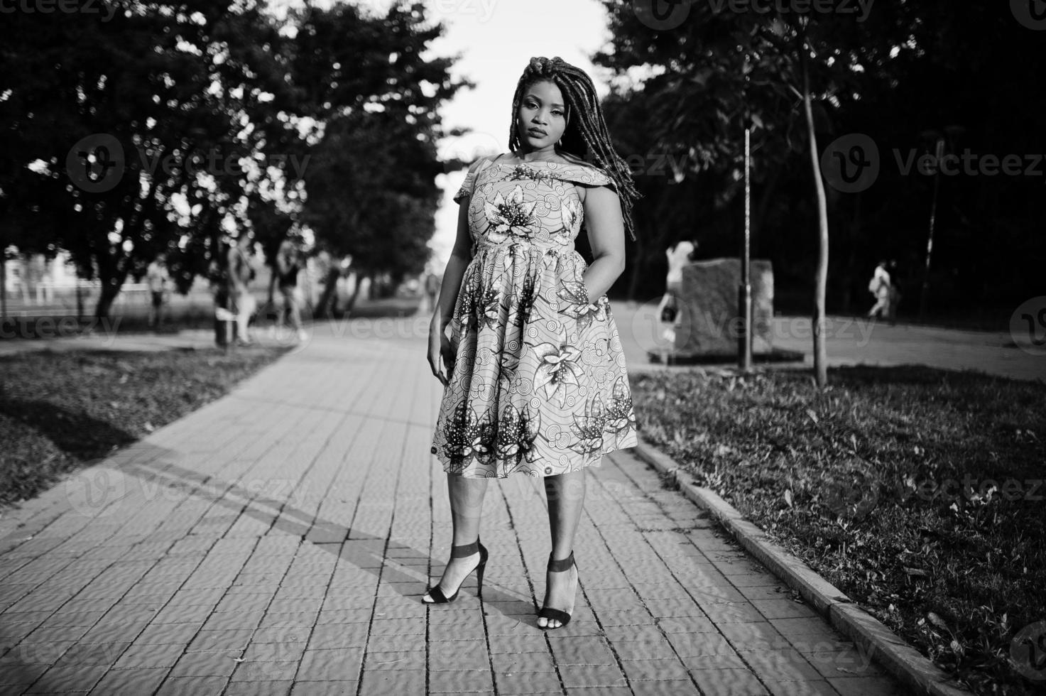 linda chica afroamericana de pequeña altura con rastas, vestida con un vestido amarillo de color, posada al atardecer. en blanco y negro. foto