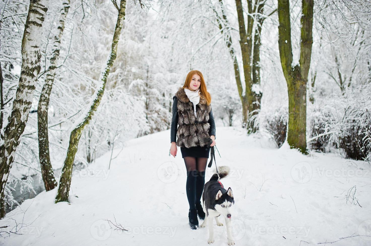 Red haired girl walking at park with husky dog on winter day. photo