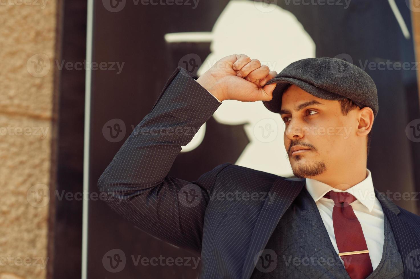 Portrait of retro 1920s english arabian business man wearing dark suit, tie and flat cap. photo