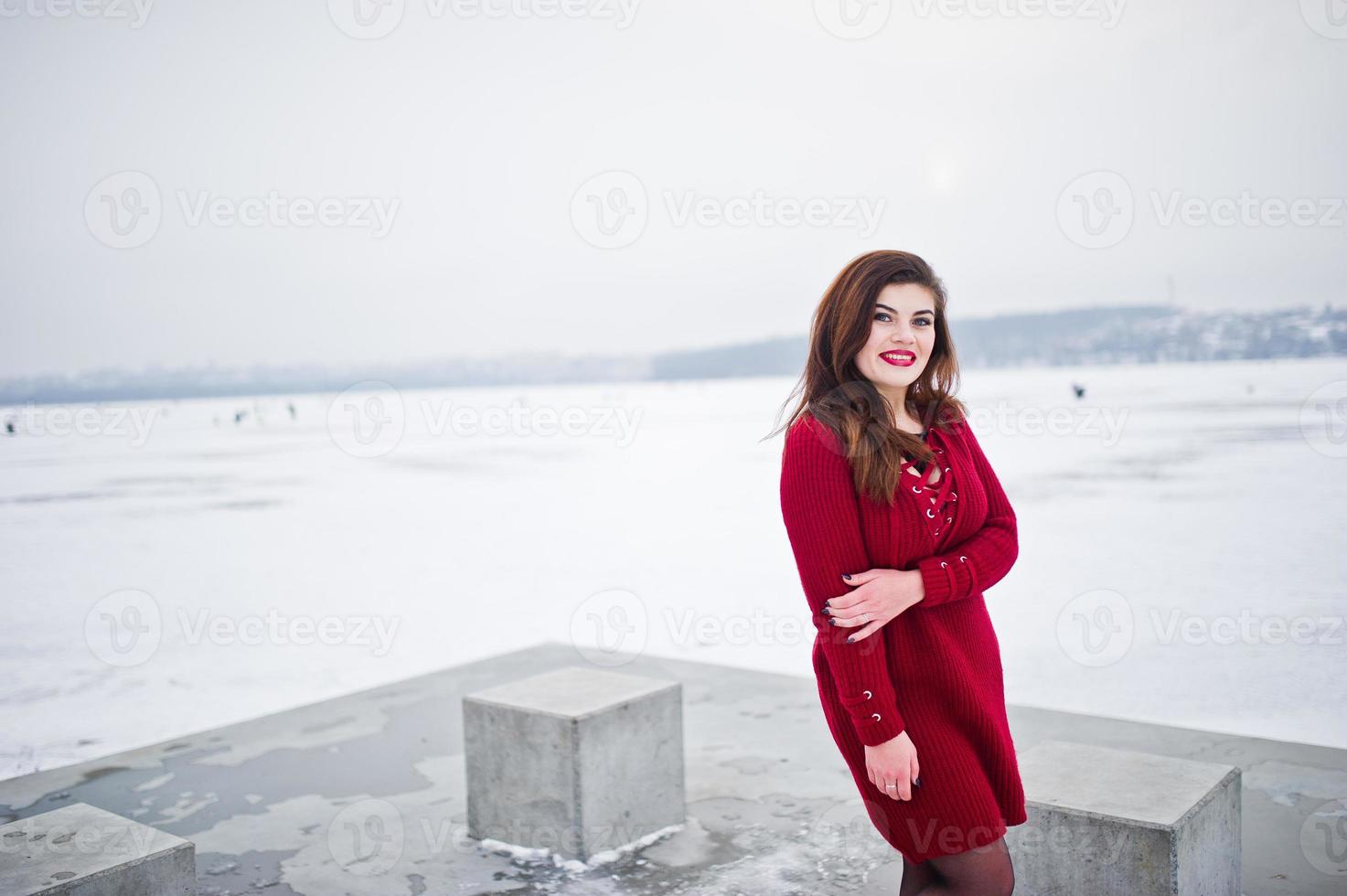 Brunette plus size model at red against frozen lake on winter day. photo