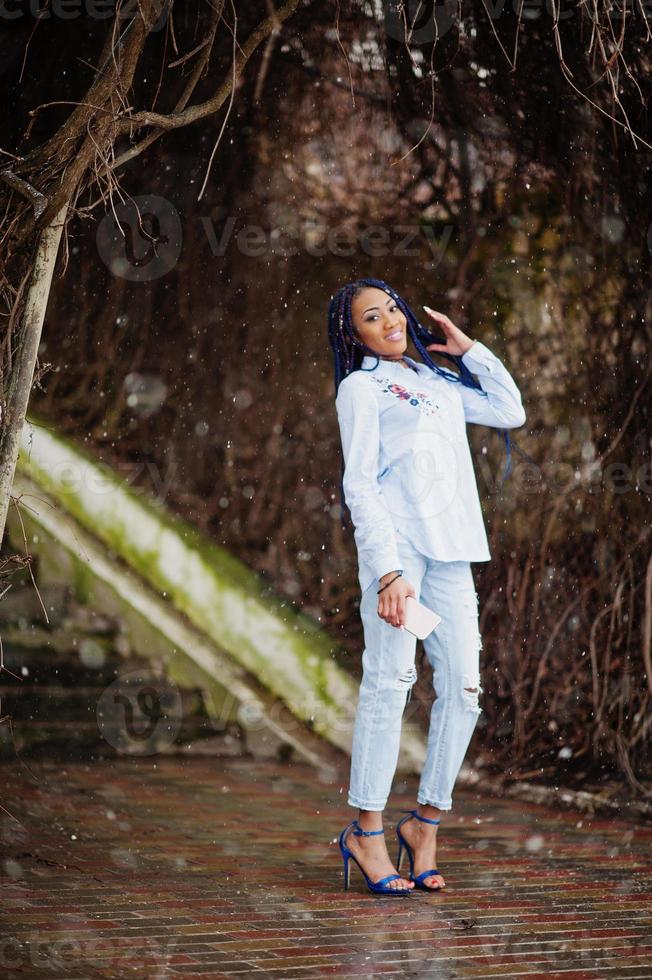 Stylish african american girl with dreads holding mobile phone at hand, outdoor snowy weather. photo