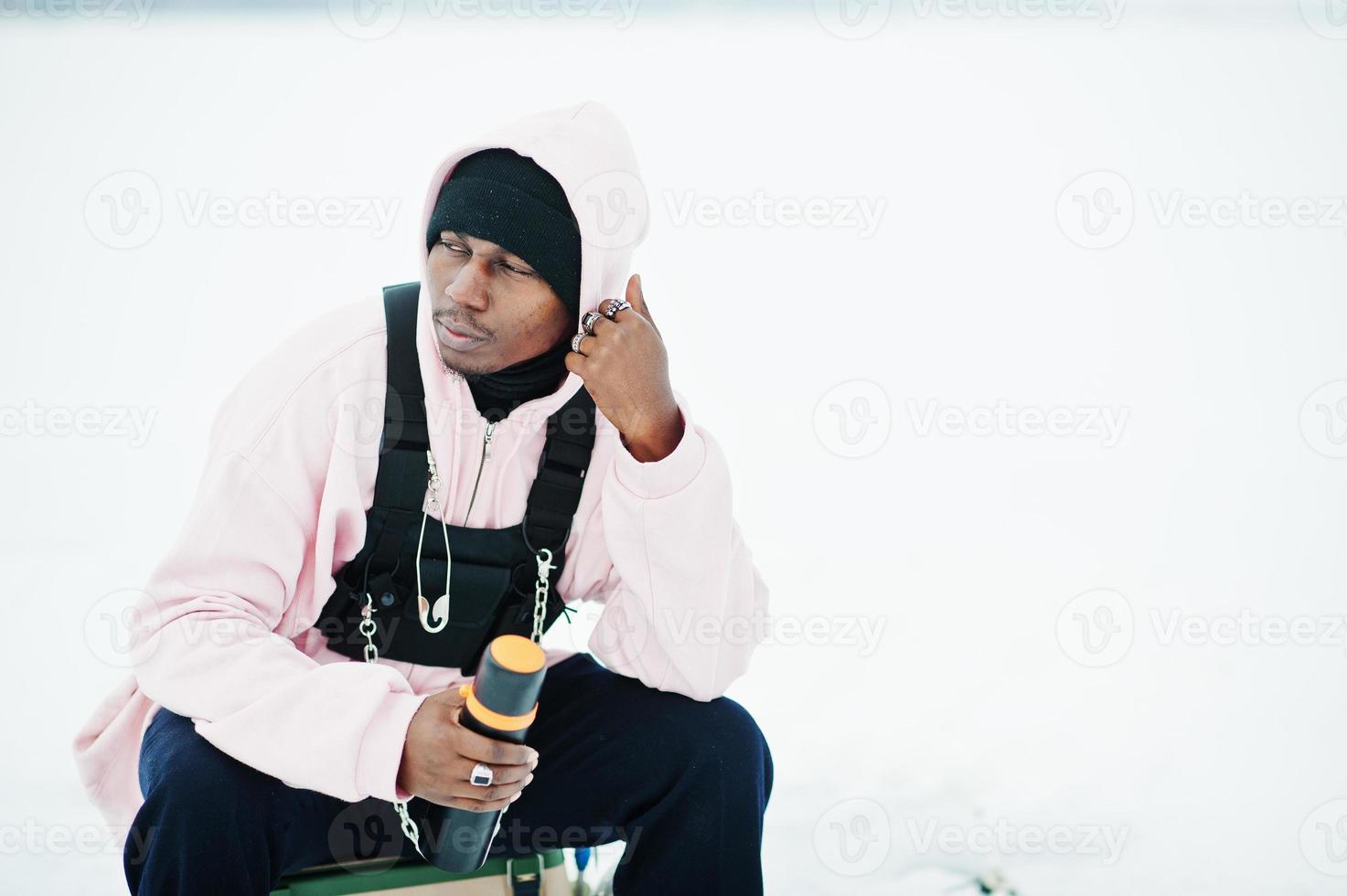 African american fisherman with thermos sitting on frozen lake. Winter fishing. photo