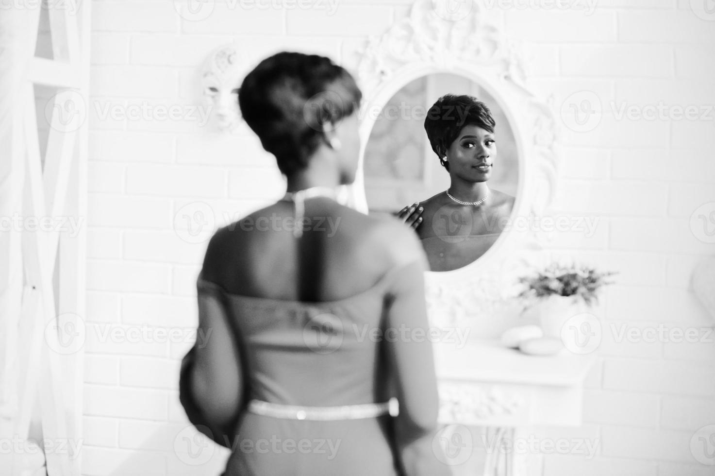 modelo afroamericano de moda en vestido de belleza rojo, mujer sexy posando vestido de noche y mirando al espejo. foto