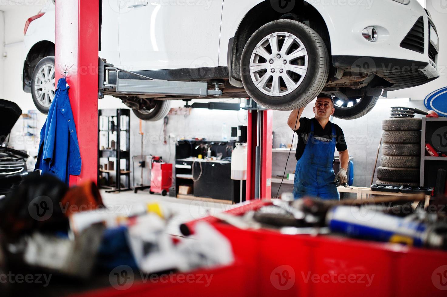 Car repair and maintenance theme. Mechanic in uniform working in auto service. photo