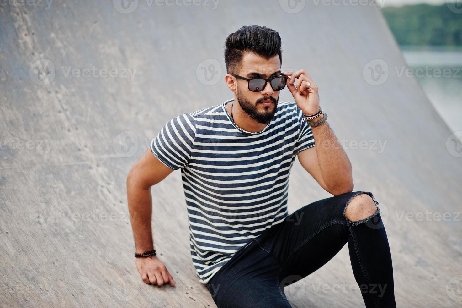 apuesto modelo de hombre de barba árabe alto en camisa despojada planteada al aire libre. chico árabe de moda en gafas de sol. foto