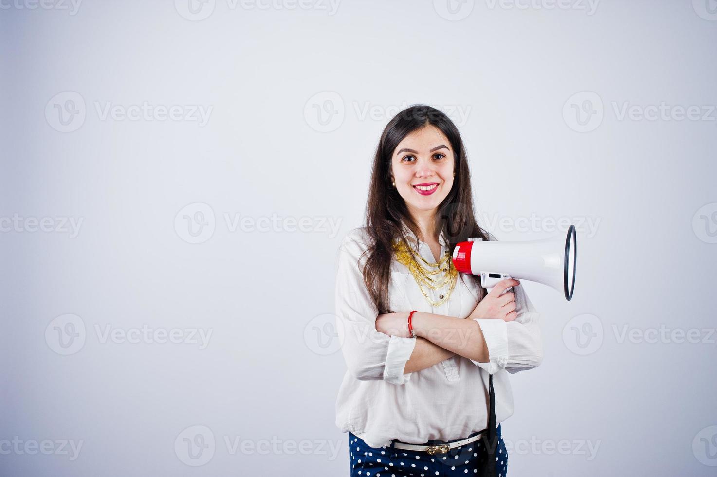 Portrait of a young woman in blue trousers and white blouse posing with megaphone in the studio. photo