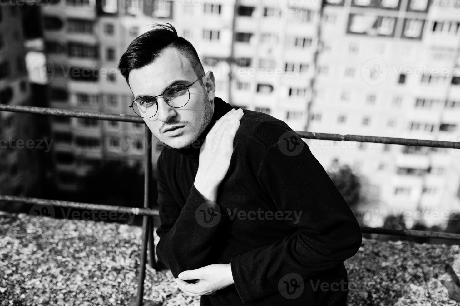 Dreamer stylish macho man in black golf and glasses posed on the roof. photo