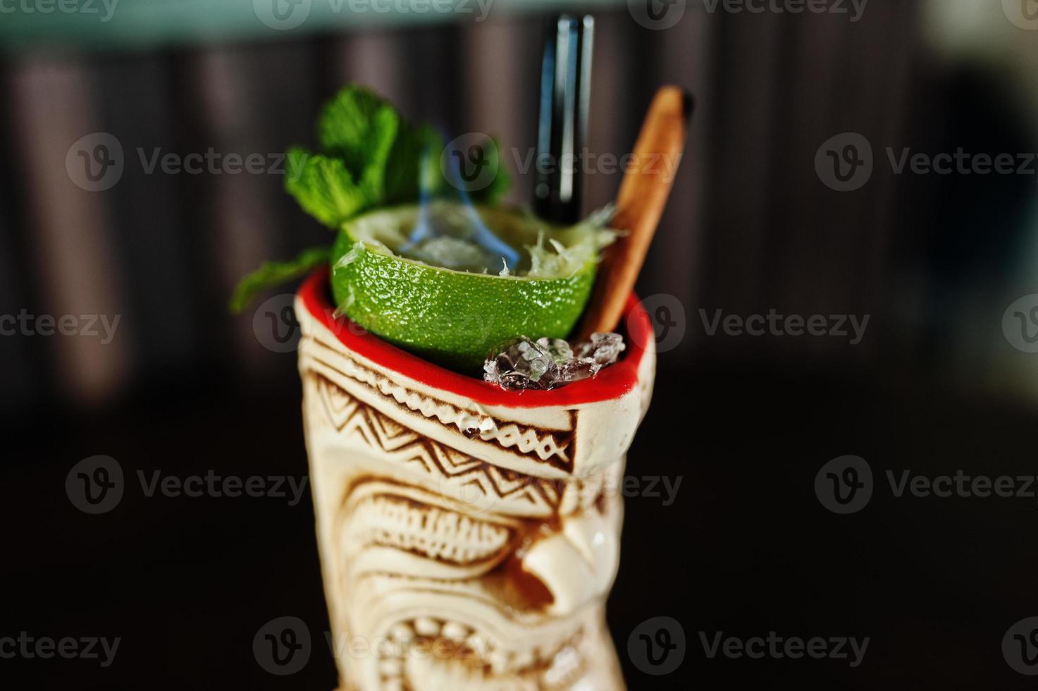 Alcoholic cocktail with mint and lime with fire in originally voodoo earthen glass on bar table. photo