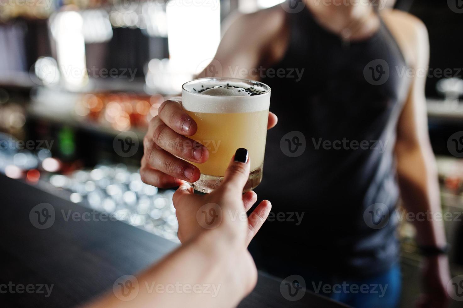 Alcoholic cocktail in glass on hand of barman gives client to drink. photo