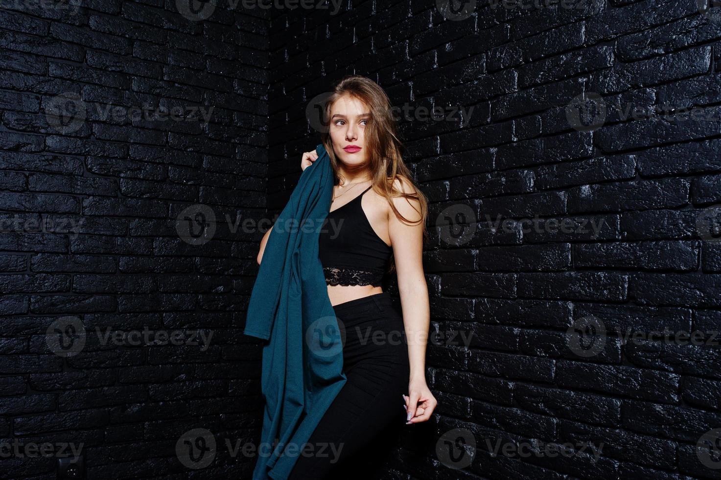 Handsome brunette girl wear on black, posing at studio against dark brick wall. Studio model portrait. photo