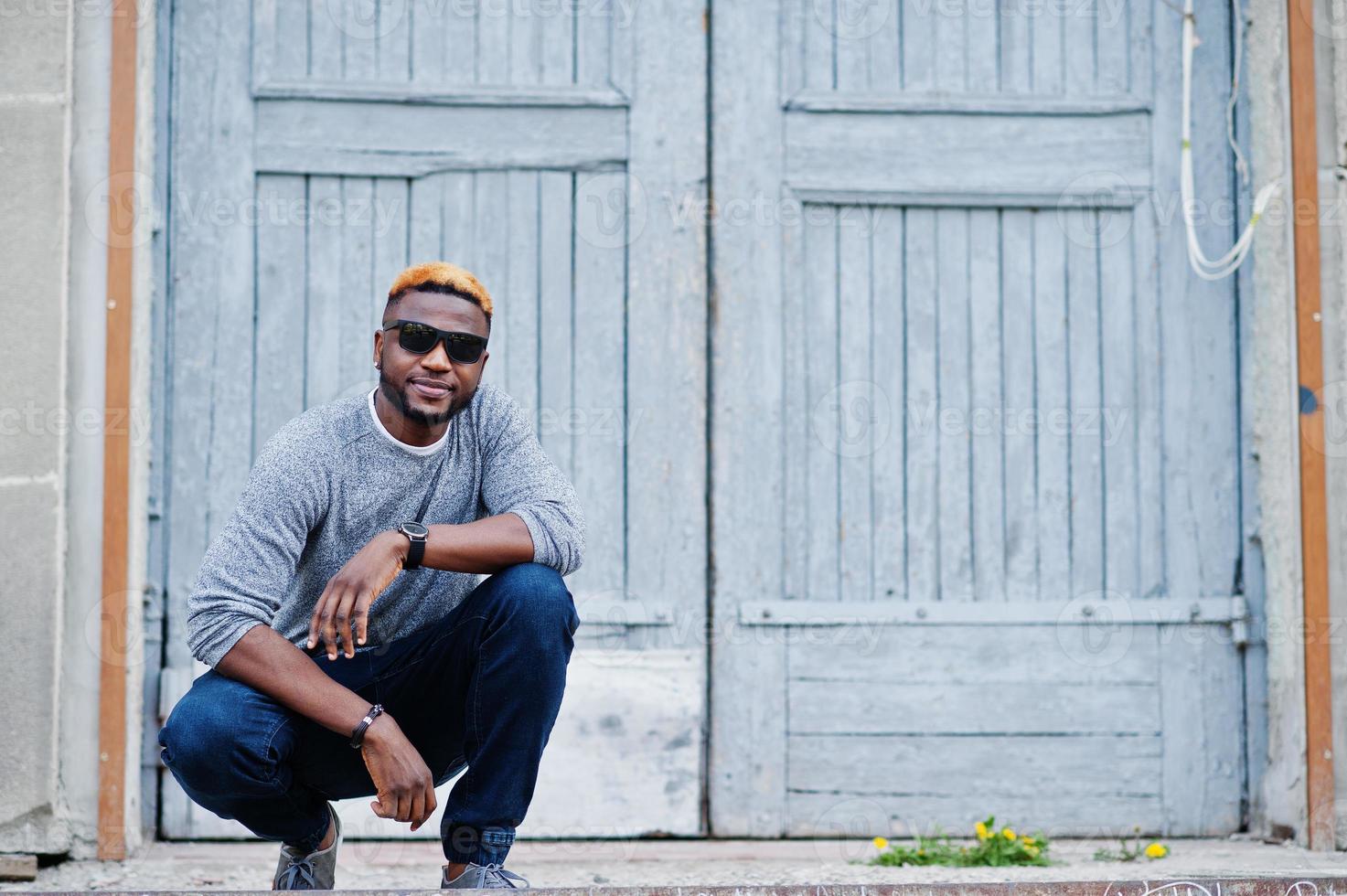 Stylish african american boy on gray sweater and black sunglasses posed on street. Fashionable black guy. photo