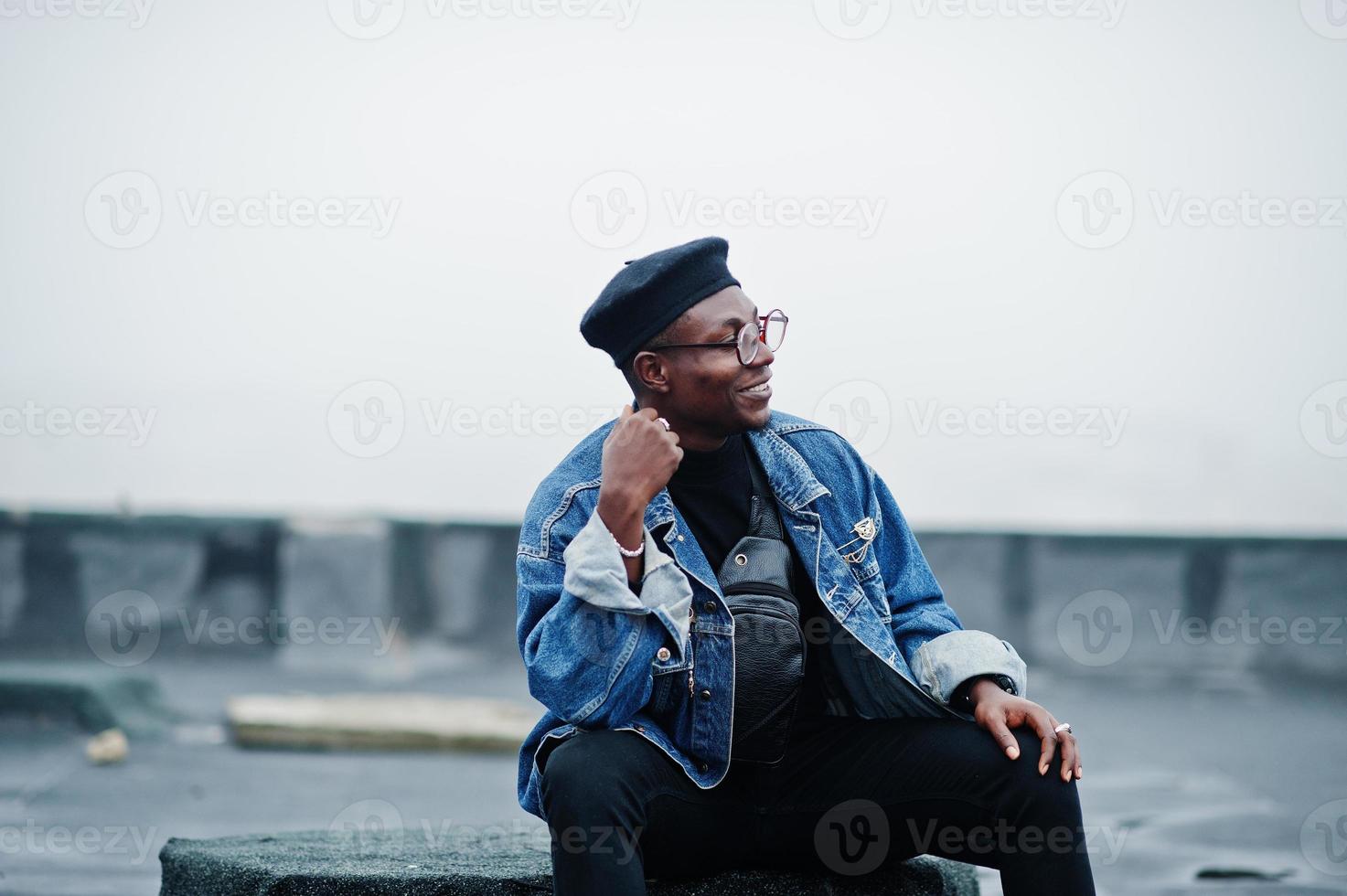 African american man in jeans jacket, beret and eyeglasses posed on abandoned roof. photo