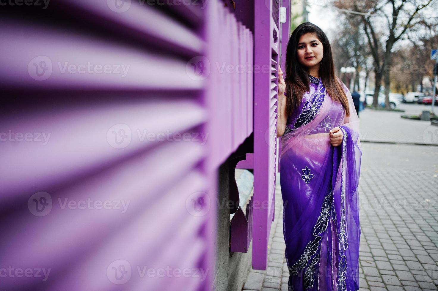 niña hindú india en el tradicional sari violeta posó en la calle contra ventanas moradas. foto