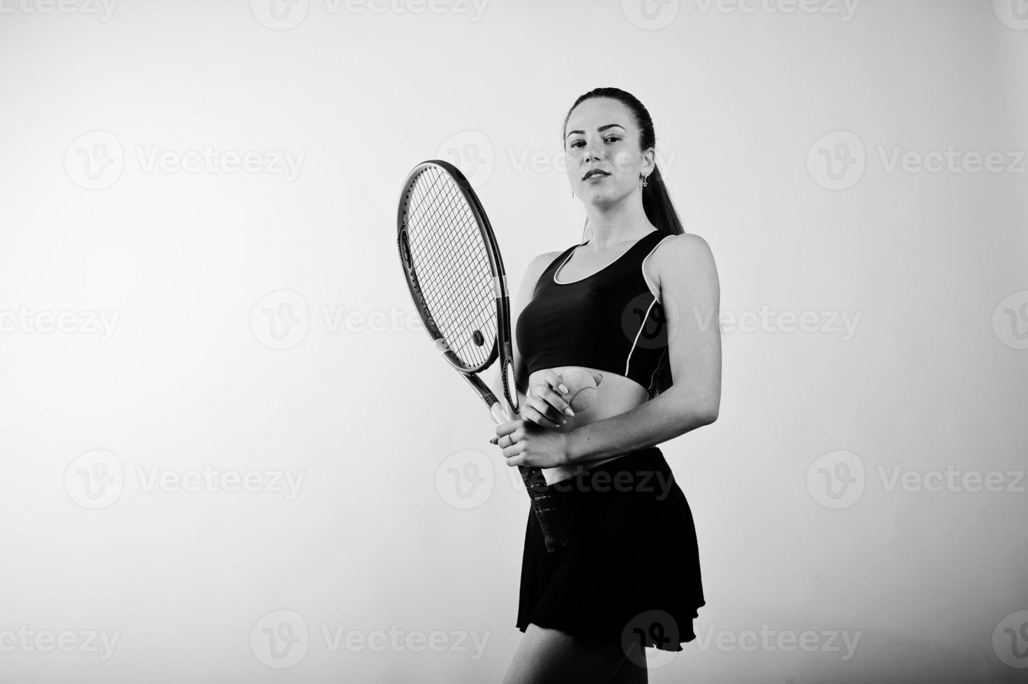 Black and white portrait of beautiful young woman player in sports clothes holding tennis racket while standing against white background. photo