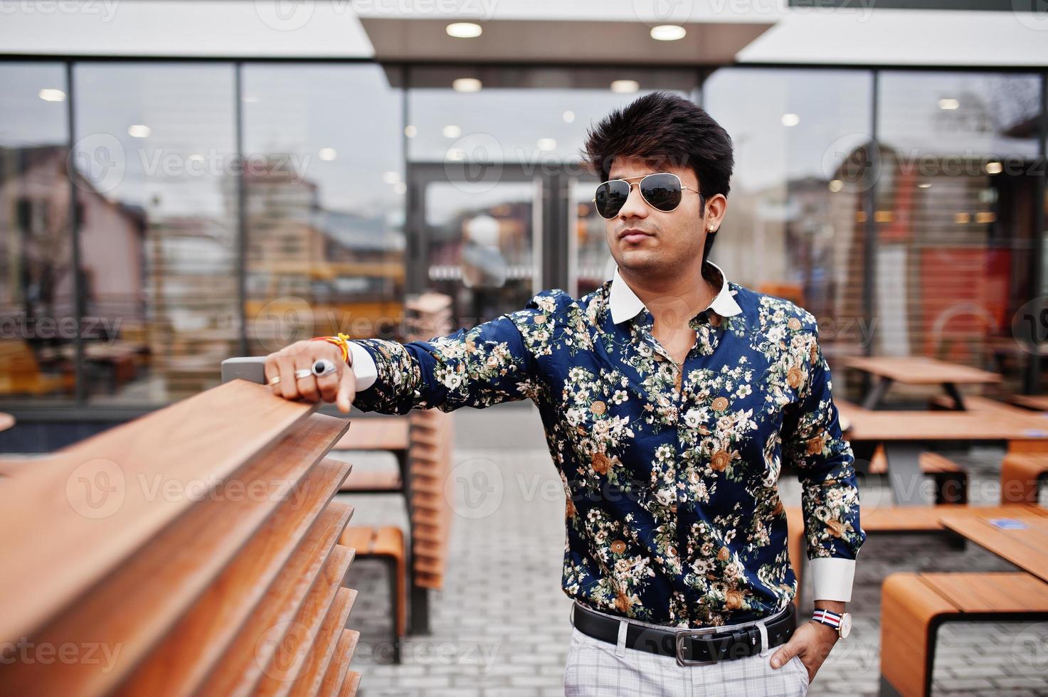 Attractive and handsome stylish indian man wear on shirt and sunglasses standing in the terrace of modern lounge cafe at his work break. photo