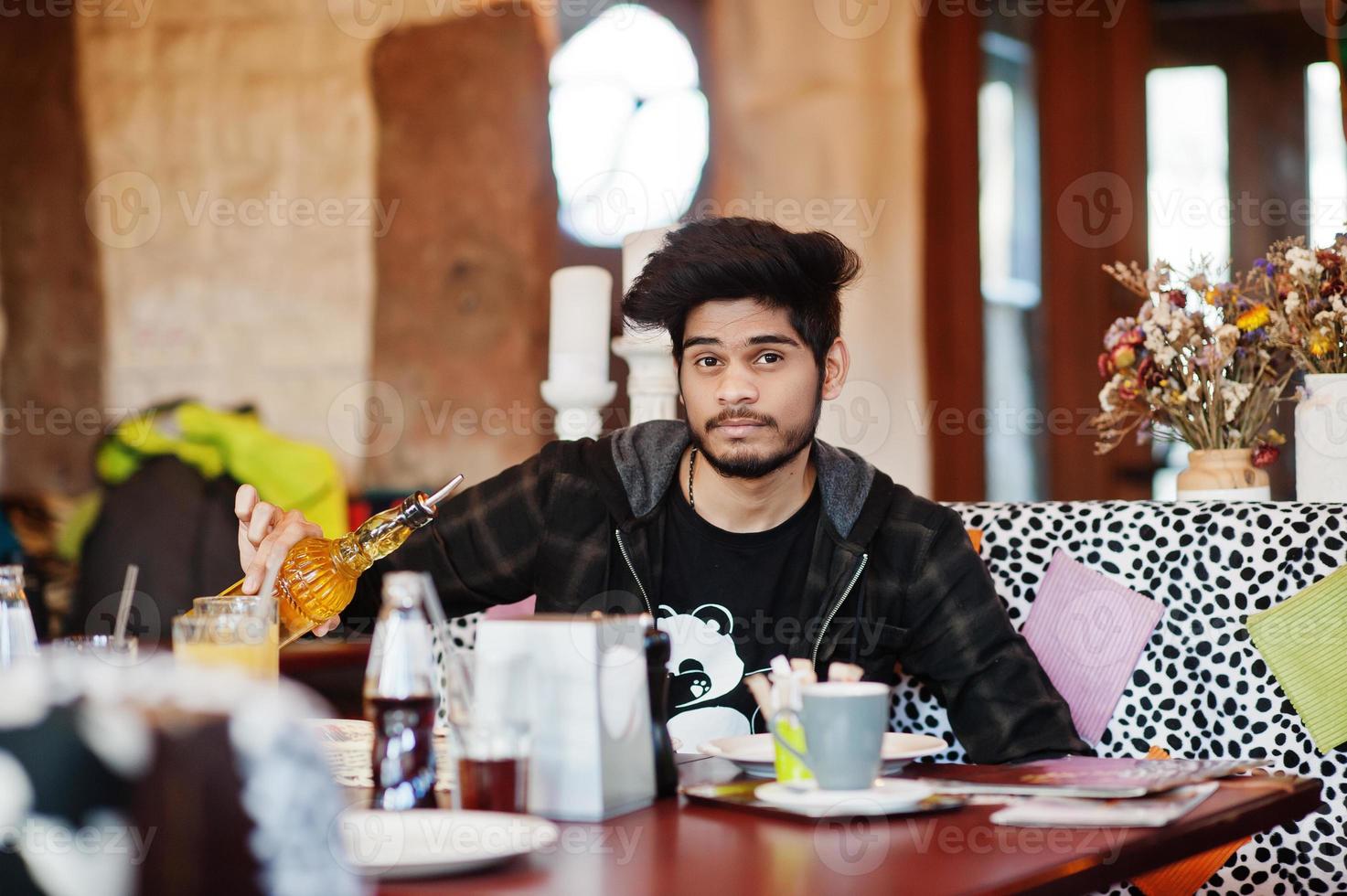 hombre asiático con barba en ropa informal sentado en un café interior y bebiendo café. foto