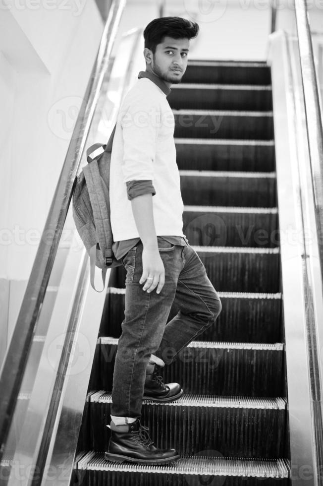 Young asian man with backpack moves on escalator at mall. photo