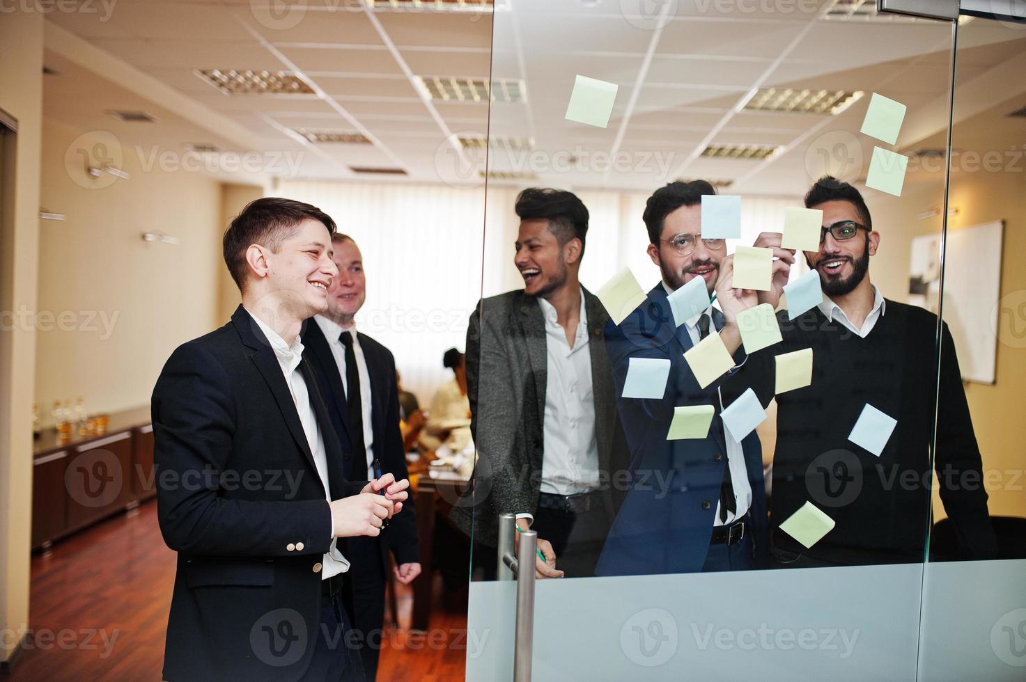 Business mans pointing on glass with colorful paper notes. Diverse group of male employees in formal wear using stickers. photo