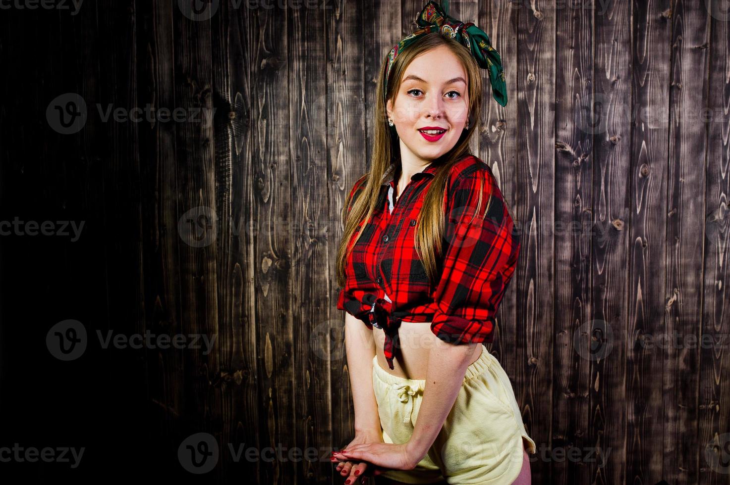 Young funny housewife in checkered shirt and yellow shorts pin up style on wooden background. photo