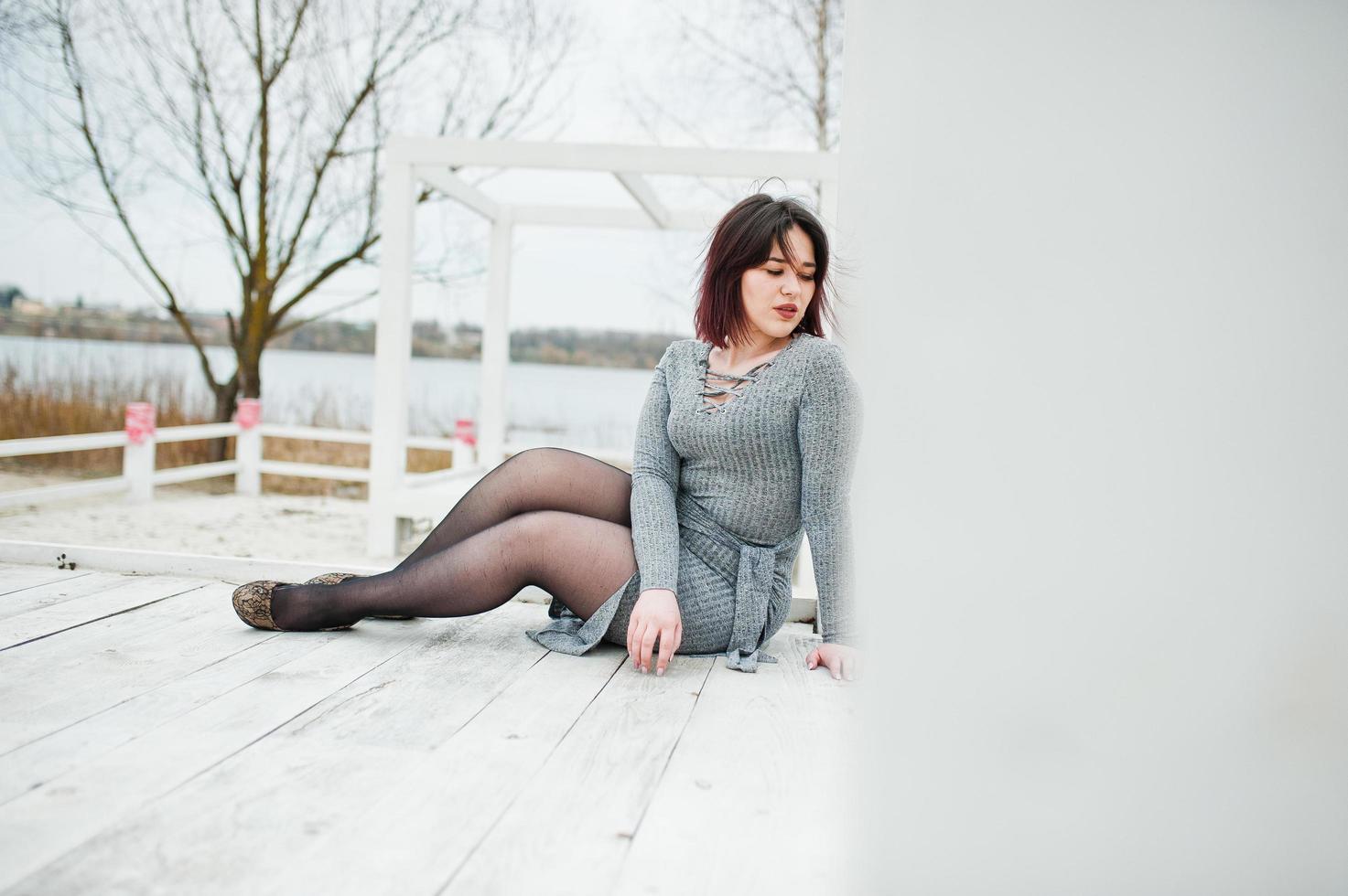 retrato de una chica morena vestida de gris sentada en una construcción de madera blanca. foto